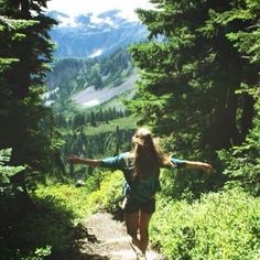 a woman with her arms outstretched walking down a trail in the woods on a sunny day