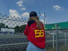 a woman standing in front of a chain link fence wearing a red shirt with the number 55 on it