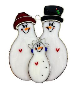 three snowmen wearing hats and scarves are hanging from a silver ornament