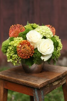 a vase filled with white and orange flowers on top of a wooden table next to a chair