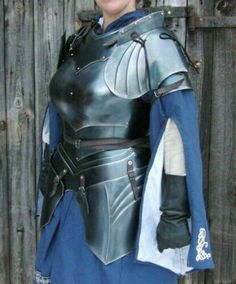 a man dressed in armor standing next to a wooden fence with his hands on his hips