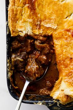 a casserole dish filled with meat and vegetables, topped with a spoon in it