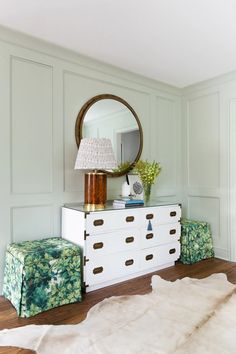 a white dresser sitting next to a mirror on top of a wooden floor in a living room