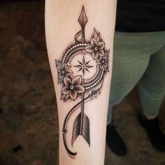 a woman's arm with an arrow and flower tattoo on the side of it