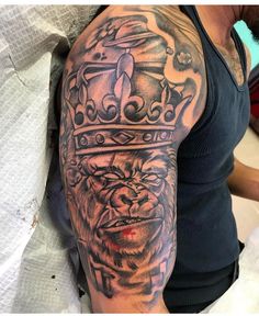 a man with a tattoo on his arm has a gorilla wearing a crown and is sitting down