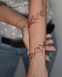 two women with matching tattoos on their arm and wrist, both holding each other's hands