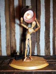 a wooden figurine holding a lamp on top of a wood table next to a striped wall