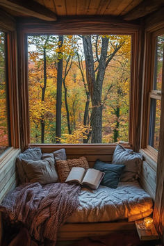 a window seat with an open book on it in front of a tree filled forest