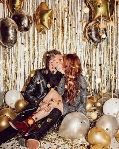 two people sitting on a couch surrounded by balloons and confetti