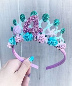 a hand holding a purple and blue tiara with flowers on it's head