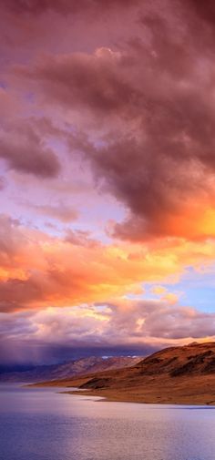 an orange and pink sky with clouds over water