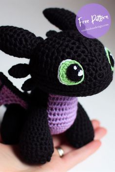 a crocheted black dragon doll with green eyes sitting on someone's hand