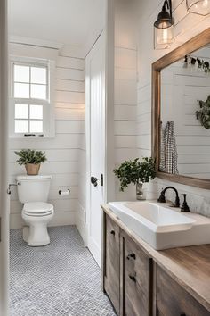 a white toilet sitting next to a bathroom sink under a mirror on top of a wooden counter