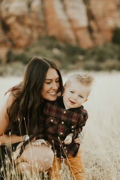 a woman holding a baby in her arms and smiling at the camera while standing in tall grass