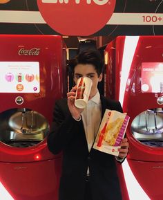 a man in a suit is eating a hot dog and drinking from a paper cup