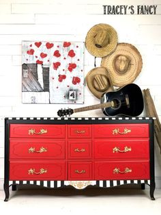 a red dresser with black and white stripes on the bottom, topped with cowboy hats