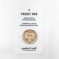 a wooden brooch with a heart on it's face and the words pocket hug written below