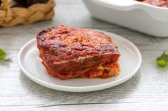 a white plate topped with lasagna next to a casserole dish filled with sauce