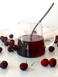 a glass pitcher filled with liquid next to cherries