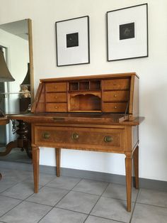 an old wooden desk with two pictures on the wall above it and a lamp next to it