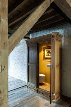 an open door leading to a toilet in a room with wooden floors and beams on the ceiling