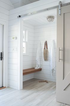 an open door leading to a white room with wooden flooring and coat racks on the wall