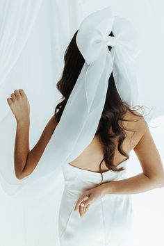 a woman wearing a white dress with a large bow on her head and veil over her hair