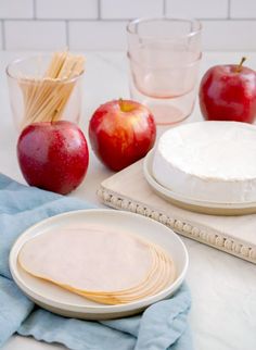 apples and cheese are sitting on the table with plates, napkins, glasses, and utensils