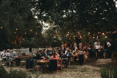 a group of people sitting at tables in the middle of a yard with string lights strung over them