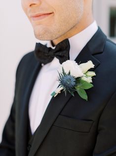 a man in a tuxedo wearing a black bow tie and white flower boutonniere