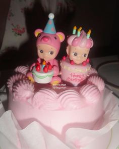 two small figurines sitting on top of a pink frosted cake with candles