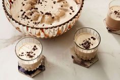 three desserts with ice cream and chocolate toppings on a marble countertop next to two glasses