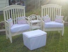 three white chairs and a footstool in the grass with pillows on them, sitting next to each other