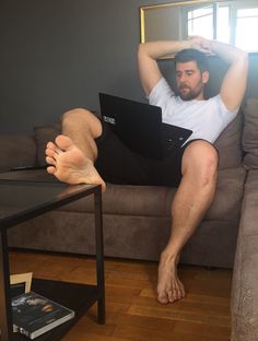 a man sitting on top of a couch with his feet up in the air while using a laptop computer