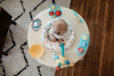 a baby is sitting in a high chair with toys around it and looking down at the floor