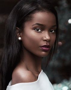 a woman with long black hair is wearing pearls on her ear and looking off to the side