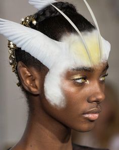 a model with white feathers on her head and gold eyeshades in the background