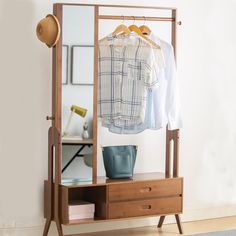 a clothes rack with two shirts and a hat on it, next to a mirror