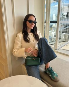 a woman sitting on a window sill holding a green purse