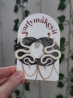 a person holding up a pair of earrings in front of a card with an image of two snakes on it