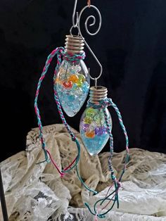 two light bulbs with colorful beads hanging from them on a wire and wrapped in twine