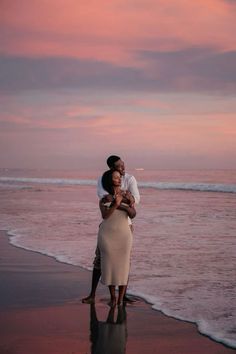 a man and woman embracing on the beach at sunset with pink clouds in the background