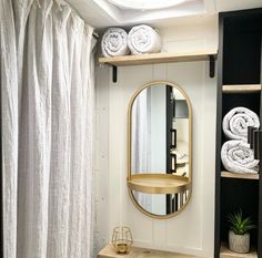 a bathroom with white towels on the shelves and a round mirror above it, in front of a curtained window