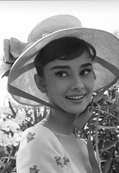 black and white photograph of a woman wearing a large hat with flowers on the side