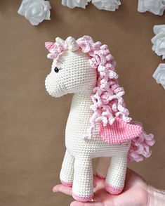 a hand is holding a small crocheted toy horse in front of white flowers