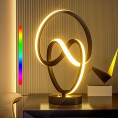 an illuminated sculpture on top of a table next to a chair and wall with a rainbow light in the background