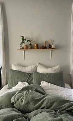 an unmade bed with green linens and pillows in front of a white wall