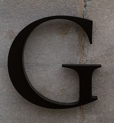 the letter c is mounted to the side of a concrete wall with a clock on it