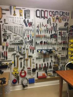 a wall full of tools hanging on the side of a wall next to a wooden table