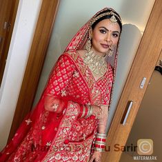 a woman in a red and gold bridal outfit posing for the camera with her hands on her hips